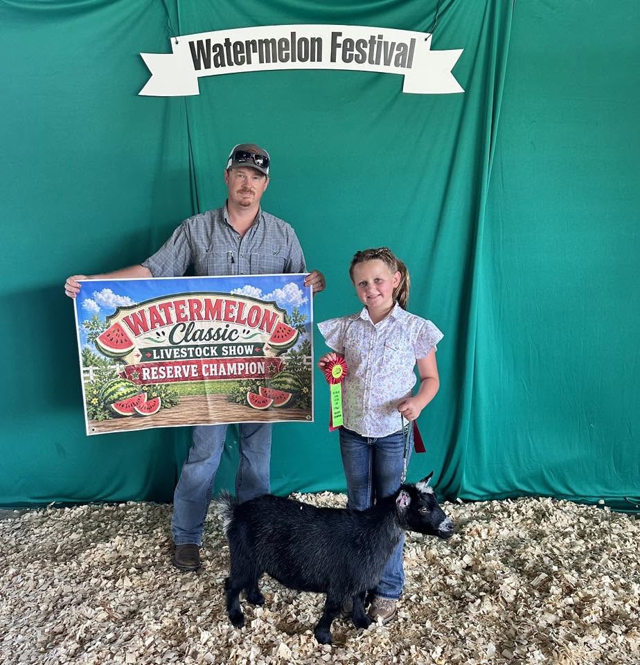 A man and a girl standing by a black goat. Watermelon Festival. Watermelon Classic Livestock Show Reserve Champion.